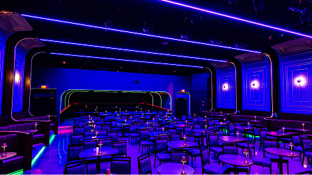 Cabaret-style interior of Greer Cabaret Theater with round tables and Theater blue stage lighting.